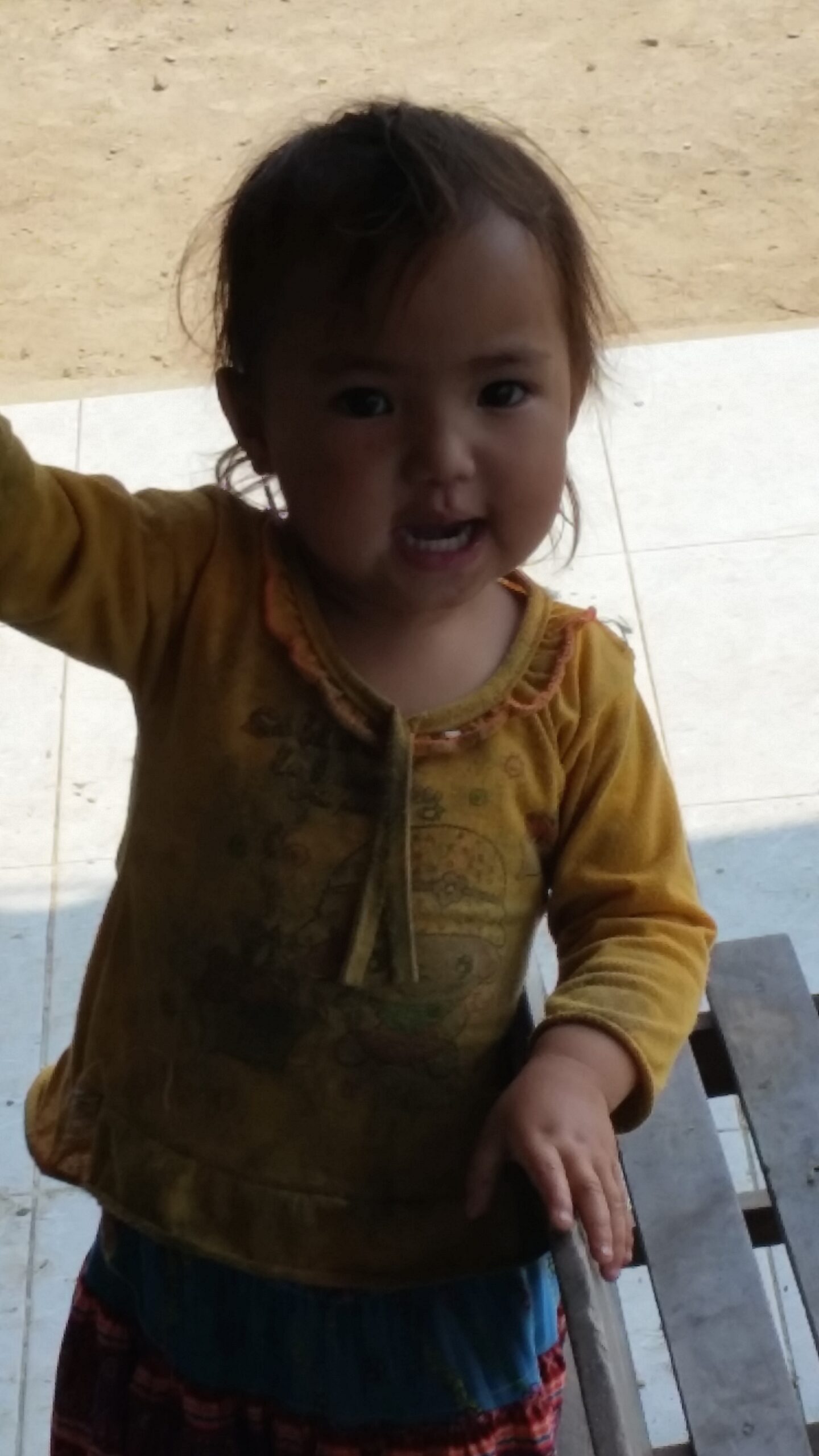 Smiling child in yellow shirt outside.