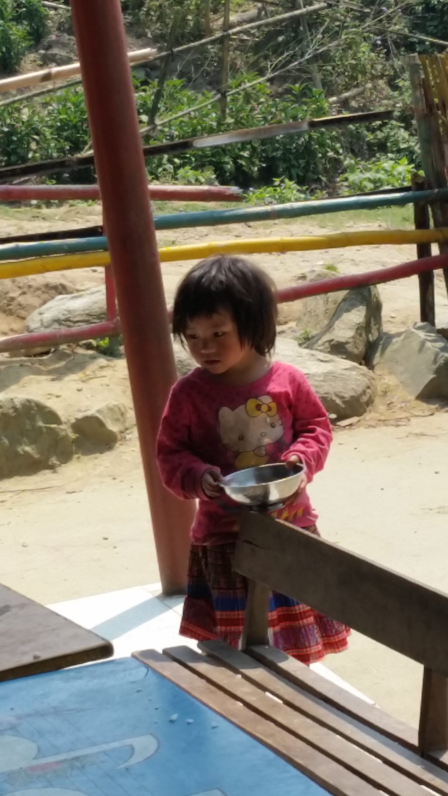 Child holding a bowl outdoors near table.