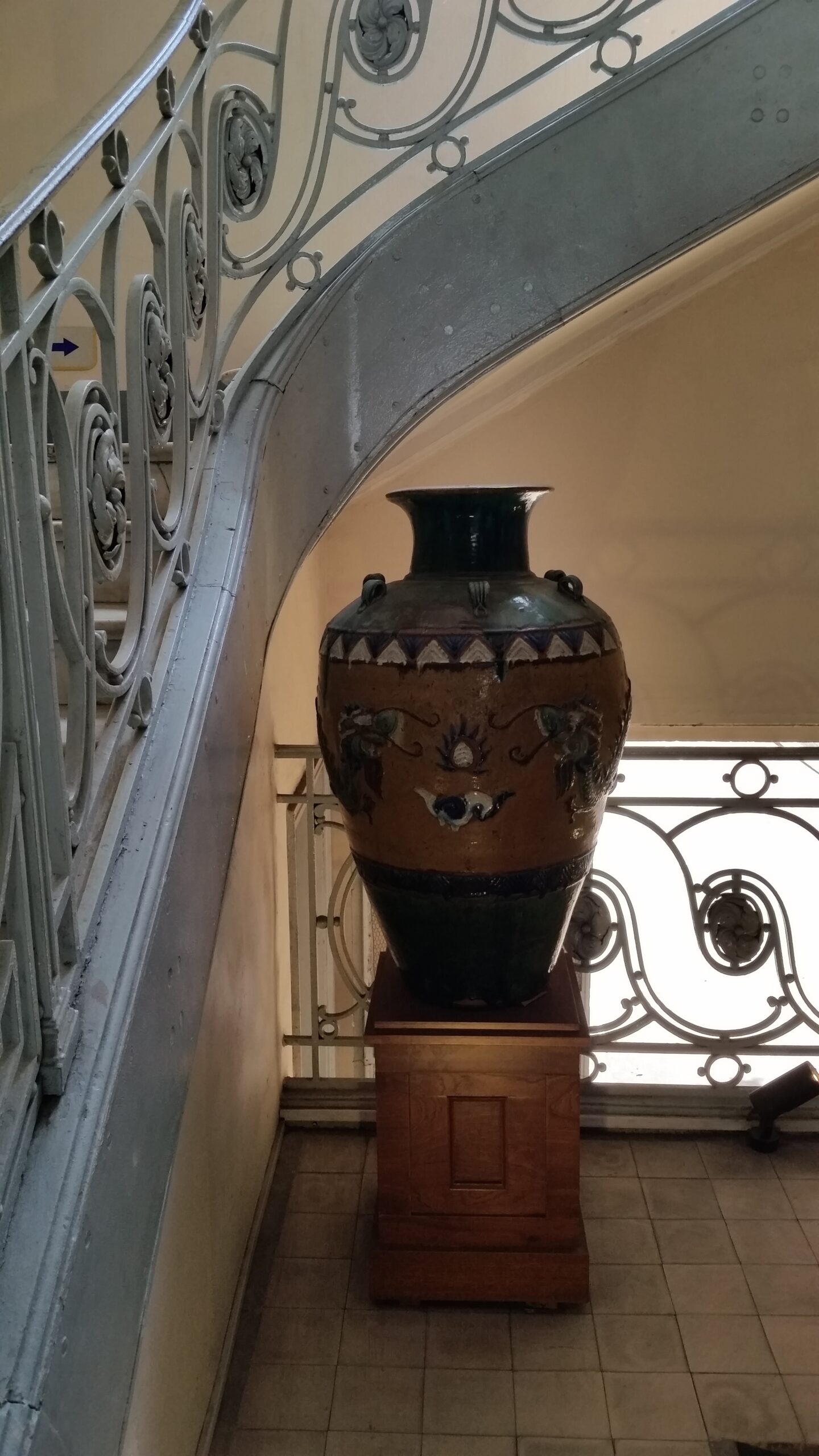 Large decorative vase under ornate staircase.
