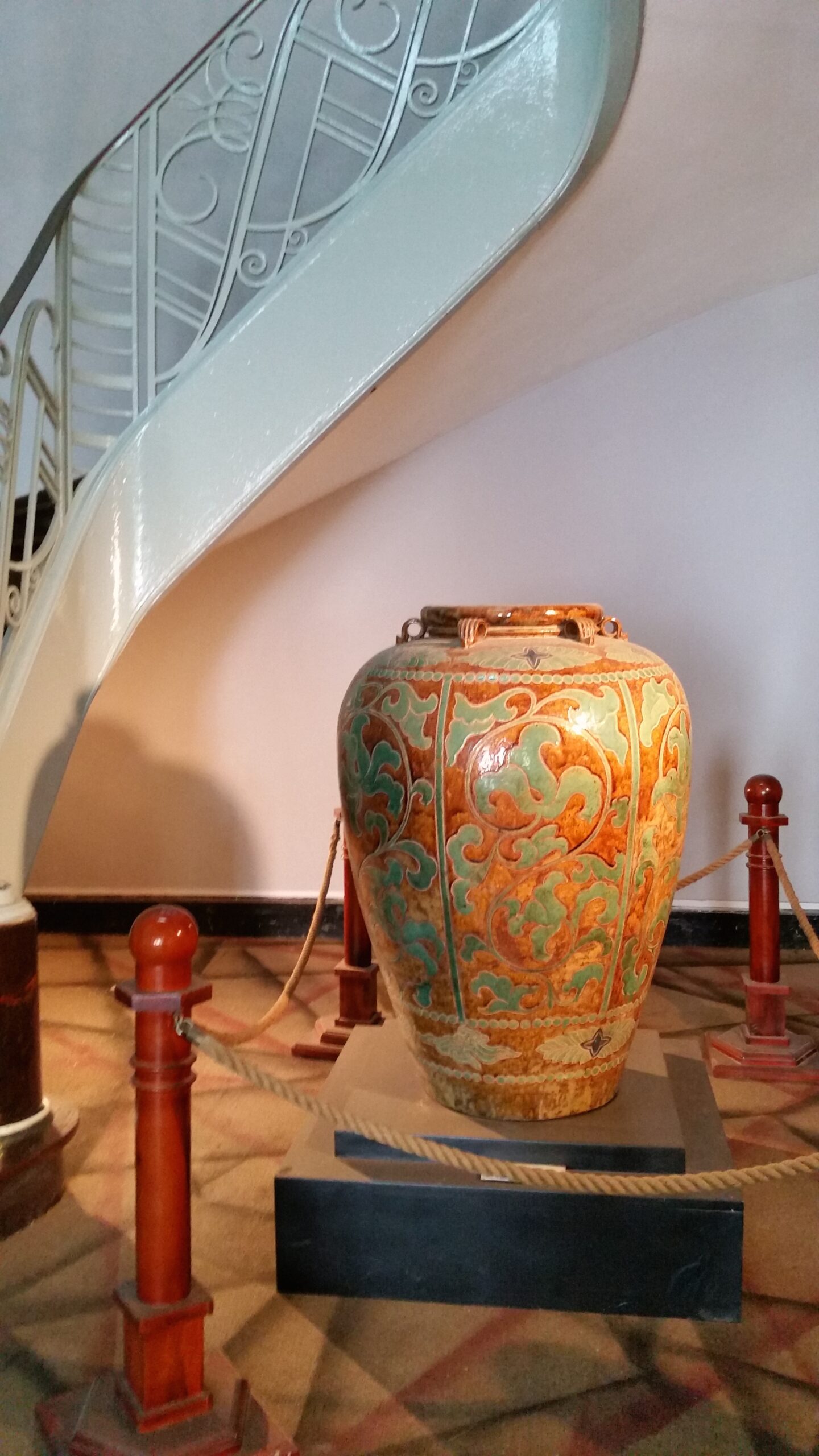 Ornate vase displayed under spiral staircase.