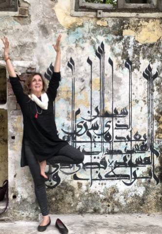 Woman posing joyfully beside calligraphy on wall.